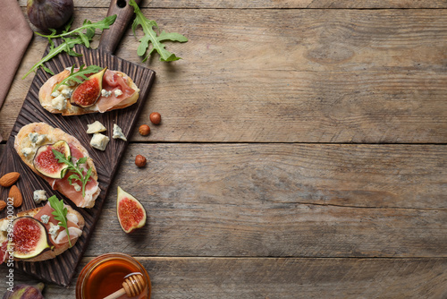 Sandwiches with ripe figs and prosciutto served on wooden table, flat lay. Space for text