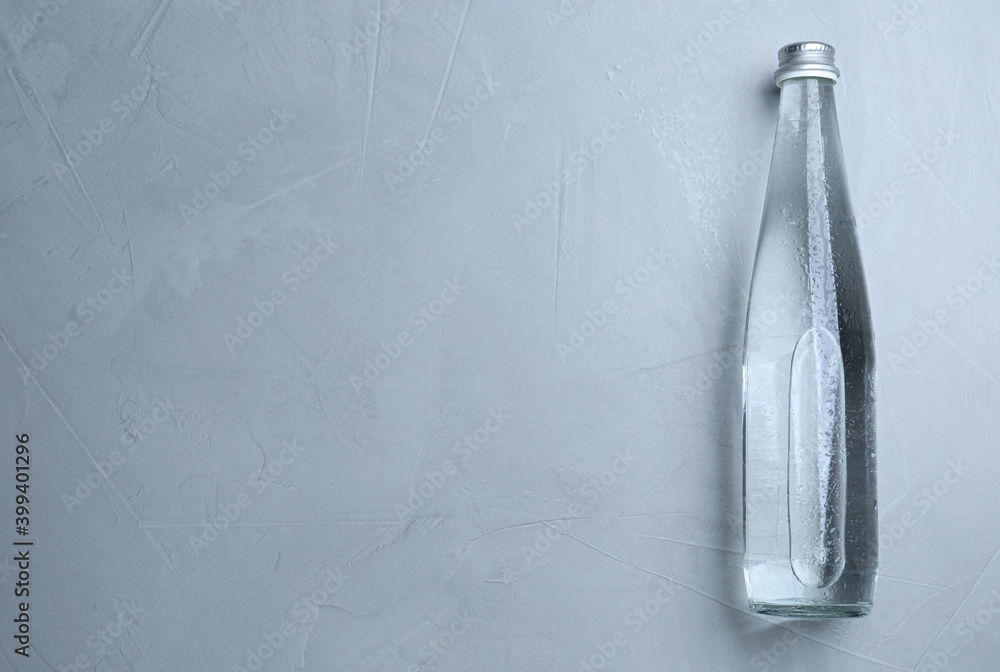 Glass bottle with water on light grey background, top view. Space for text Glass bottle with water on light grey background, top view. Space for text