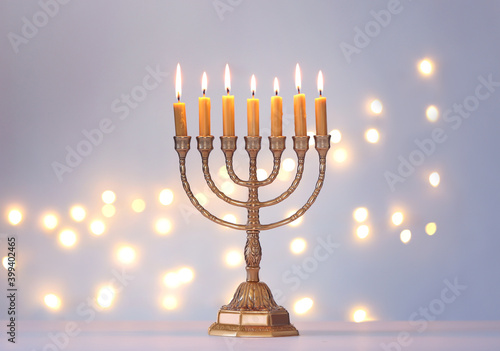 Golden menorah with burning candles against light grey background and blurred festive lights