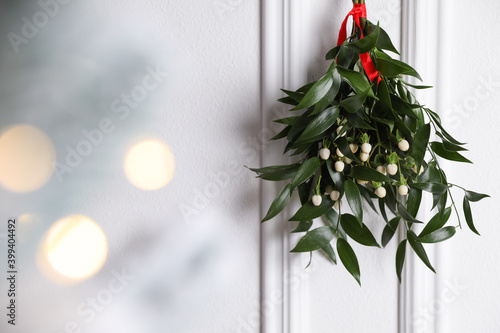 Vászonkép Mistletoe bunch with red ribbon hanging on light background, space for text