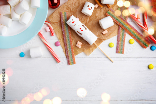 Flat lay composition with funny snowman made of marshmallows on white wooden table, space for text. Bokeh effect