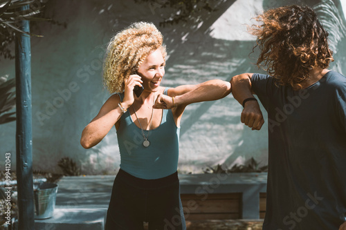 Smiling woman giving elbow bump to man while talking on mobile phone outdoors photo