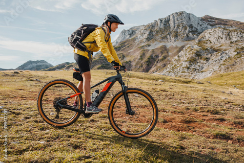 Mid adult woman with backpack riding bicycle on mountain at Somiedo Natural Park, Spain photo