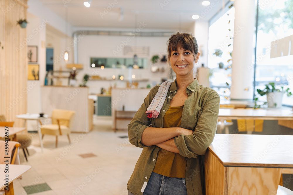 Female owner with arms crossed napkin on shoulder standing in coffee shop Female owner with arms crossed napkin on shoulder standing in coffee shop