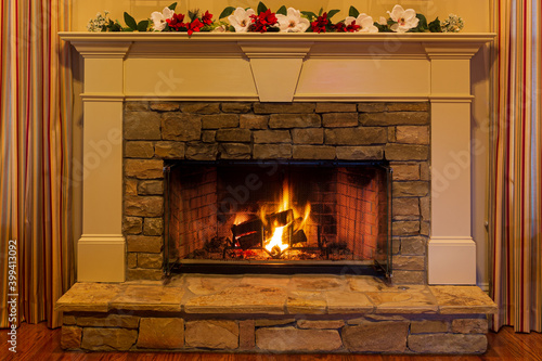 Glowing fire in a stone fireplace decorated with red and white flowers.