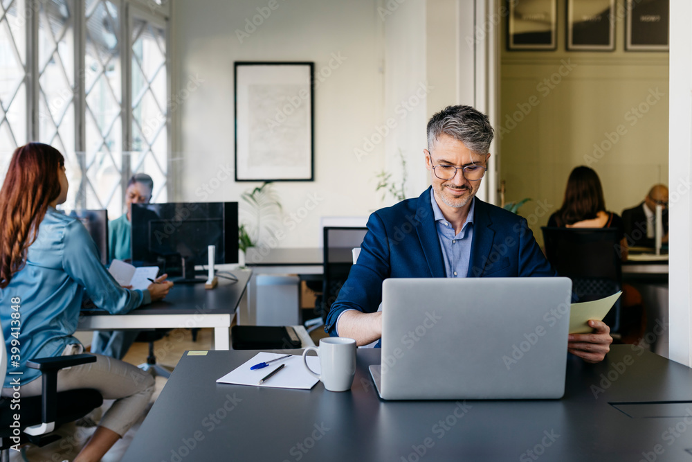 Smiling businessman working on laptop at desk in office Smiling businessman working on laptop at desk in office