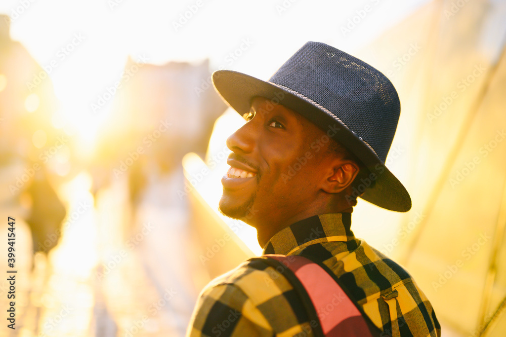 Smiling african man with backpack in city during sunset Smiling african man with backpack in city during sunset