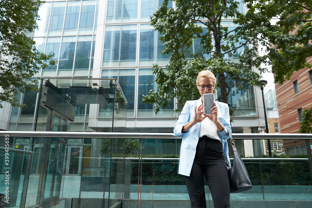 Mature woman using mobile phone while leaning on railing in city Mature woman using mobile phone while leaning on railing in city