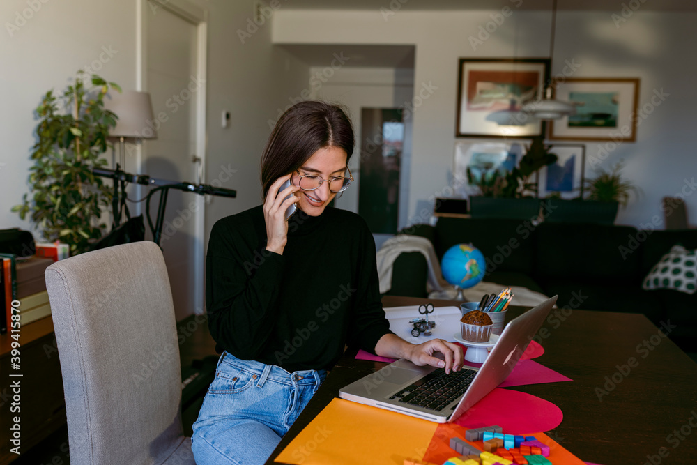 Female freelancer talking on smart phone while using laptop sitting at home Female freelancer talking on smart phone while using laptop sitting at home