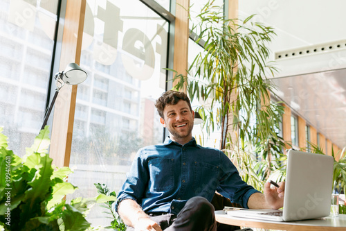 Cheerful young businessman looking away while sitting with laptop at table in cafe