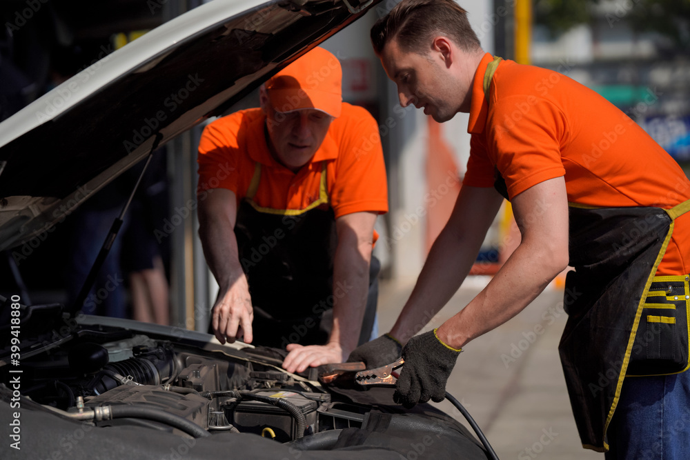 Two men are car mechanic Use a wrench and a cord to check the car battery. Two men are car mechanic Use a wrench and a cord to check the car battery.