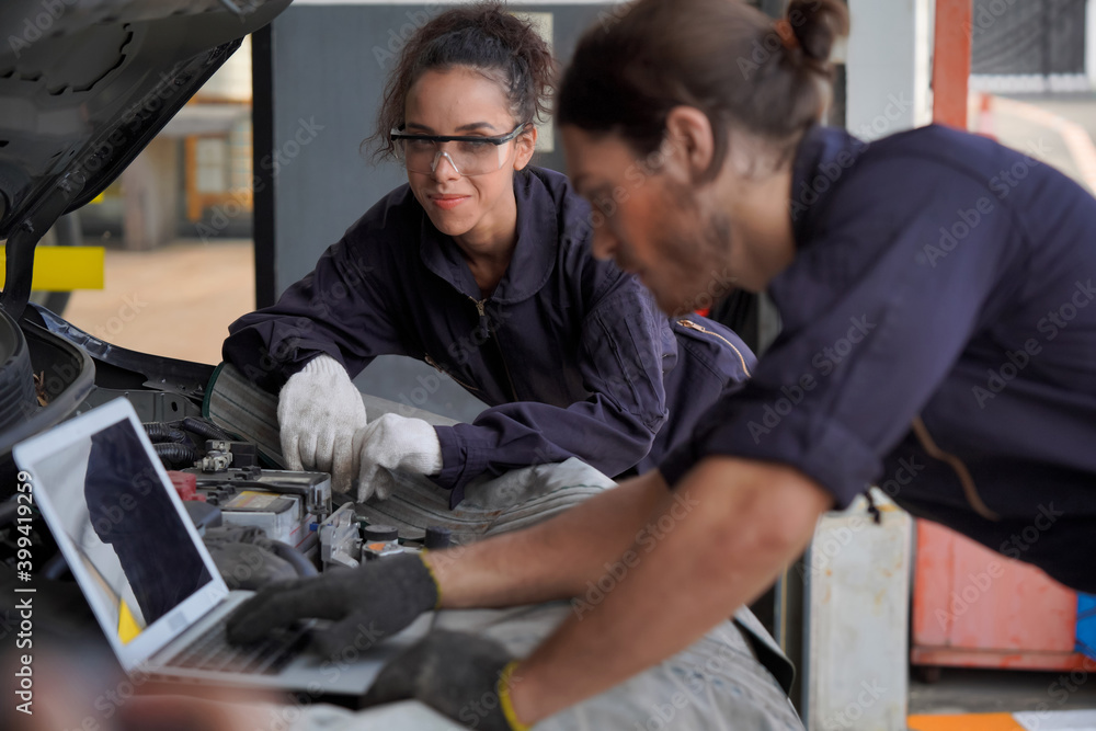 Two young men and women car mechanic I am using a laptop to check and condition the engine.