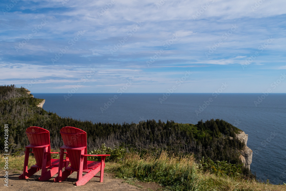 Two red Adirondack chairs facing the sea in the Forillon national park, Canada