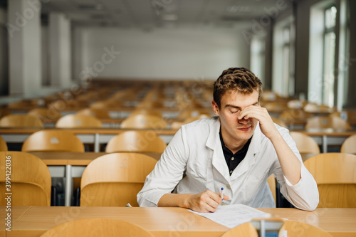 Medical professional filling out a document, looking exhausted, tired. Anxious doctor writing an opinion.Medicine exam, medical practitioner taking test evaluation. Stressed male nurse student © eldarnurkovic