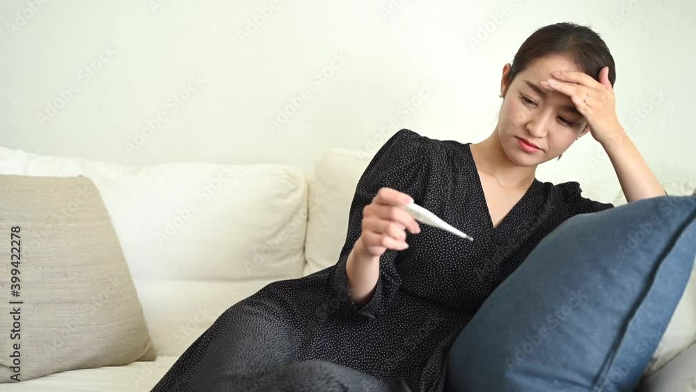 体温計を見ながらソファーに寄り掛かかる体調不良の女性