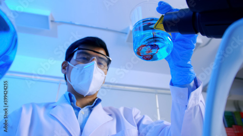 Asian scientist doing some research checking a liquid in a test flask at laboratory.