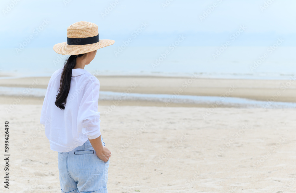 Outdoor summer portrait of young asian woman in straw hat looking to the sea at tropical beach, enjoy freedom time, fresh air and leisure travel vacation.