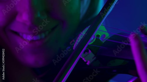 Detailed footage of a wooden violin and bow. A professional violinist plays a classical symphony against a backdrop of bright neon lights. Woman face and sliver tool close up. Slow motion.