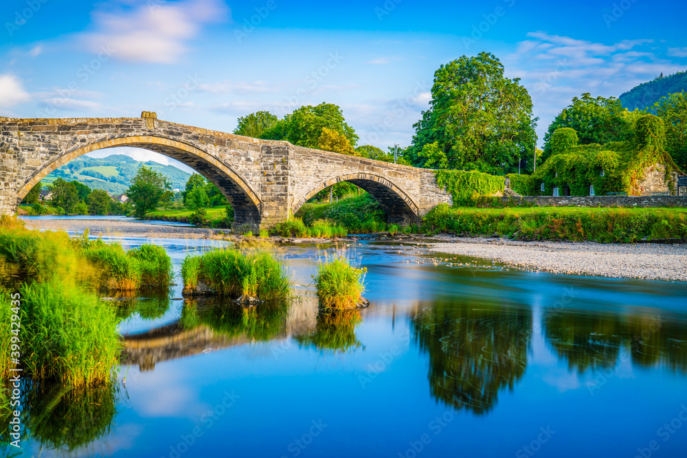 Fototapeta premium Stone bridge across the river Conwy and old cottage covered with vine leaves, Llanrwst, Caernarfon, North Wales