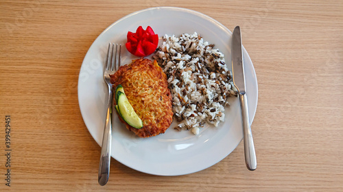 Breakfast on a plate on the table, a fork with a knife, porridge and cutlet, a slice of tomato and cucumber