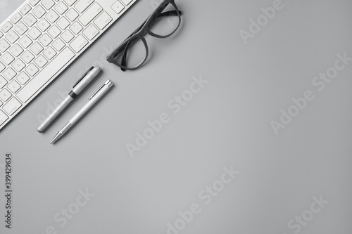 top view of workspace with glasses, 2 pens and a white keyboard in a gray background with copy space