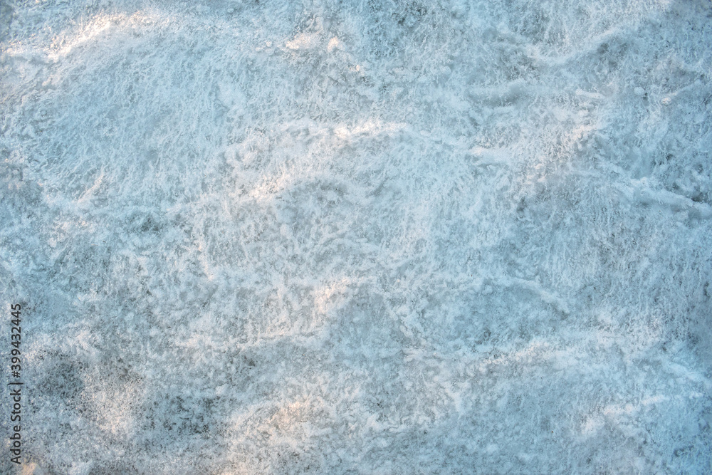 Sea ice texture. Frozen sea water with congealed small bubbles inside. The sea ice is pale blue. Embossed sea ice illuminated by the setting sun