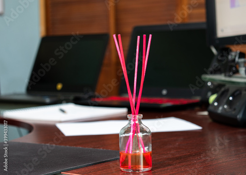 Botella de cristal aromatizante con varillas de color rosa sobre un escritorio. Home Office. photo
