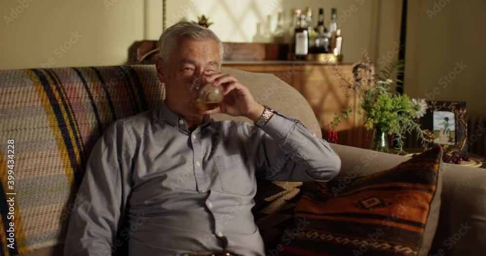 4k, Senior man relaxing on the sofa at home with a glass of whiskey in the evening 4k, Senior man relaxing on the sofa at home with a glass of whiskey in the evening