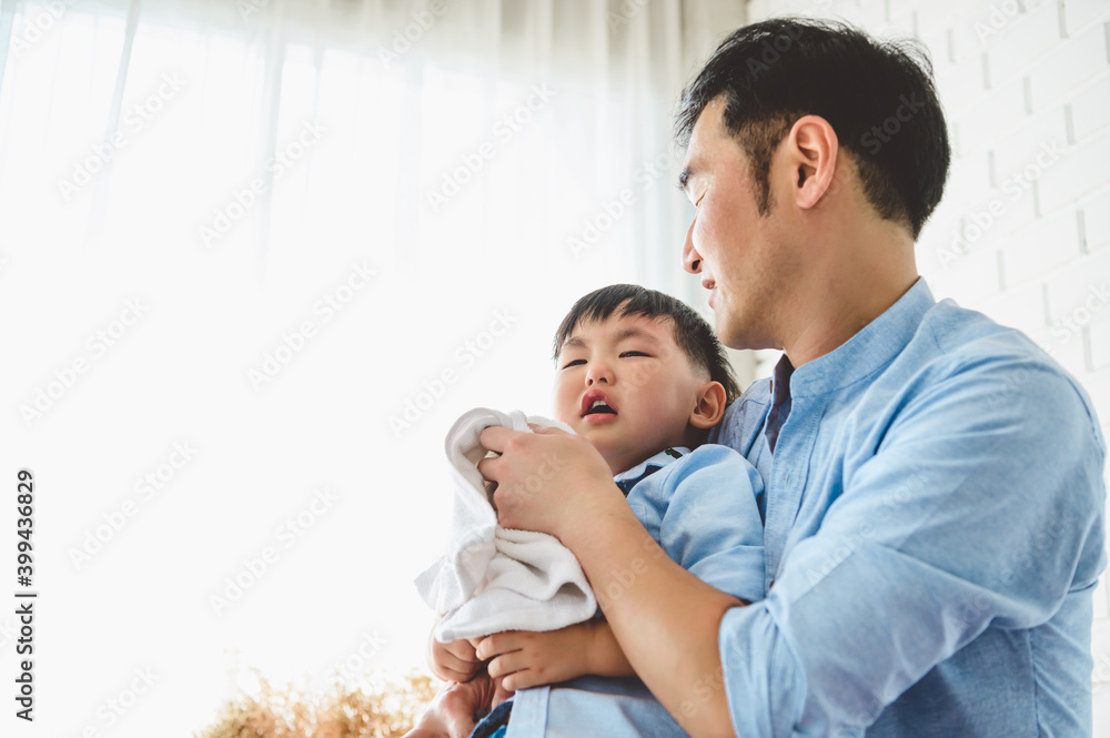 Asian Japanese father consoling his crying son and wiping tears in bedroom at his home white curtain background. People lifestyle health. Medical and Health concept. Negative emotion theme. Asian Japanese father consoling his crying son and wiping tears in bedroom at his home white curtain background. People lifestyle health. Medical and Health concept. Negative emotion theme.