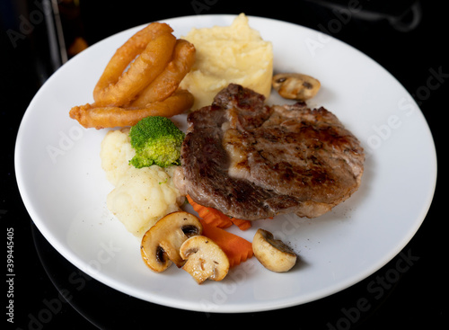 Rib eye beef steak with mashed potatoes mushrooms, onion rings. Served with pepper sauce