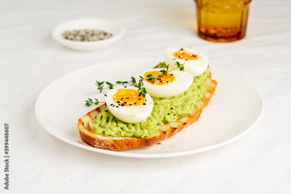 Avocado toast with toasted bread soft-boiled eggs with yellow yolk and tomatoes with herbs on white plate on light tablecloth Avocado toast with toasted bread soft-boiled eggs with yellow yolk and tomatoes with herbs on white plate on light tablecloth