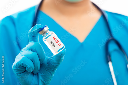 Female nurse with stethoscope puts on rubber gloves and wearing medical face mask, woman doctor in blue uniform holding COVID-19 vaccine, isolated on over white background, medical health concept