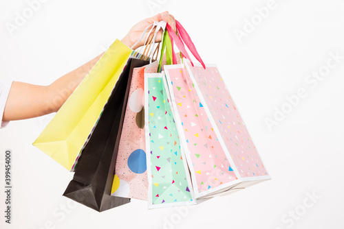 Closeup women hand holding colorful multicolor shopping bag many packets isolated on white background, female holds in hand white clear empty blank craft paper gift bag, shopping day concept