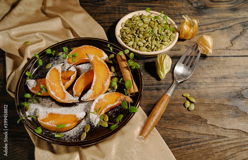 Baked pieces of pumpkin in powdered sugar with mint leaves in a ceramic plate with seeds and a fork on a wooden table. Autumn menu. Diet. photo