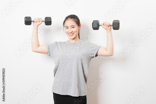 Beautiful young Asian woman lifting dumbbells smiling and energetic isolated over white background. Healthy lifestyle.