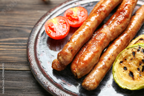 Plate with delicious grilled sausages and vegetables on wooden table, closeup