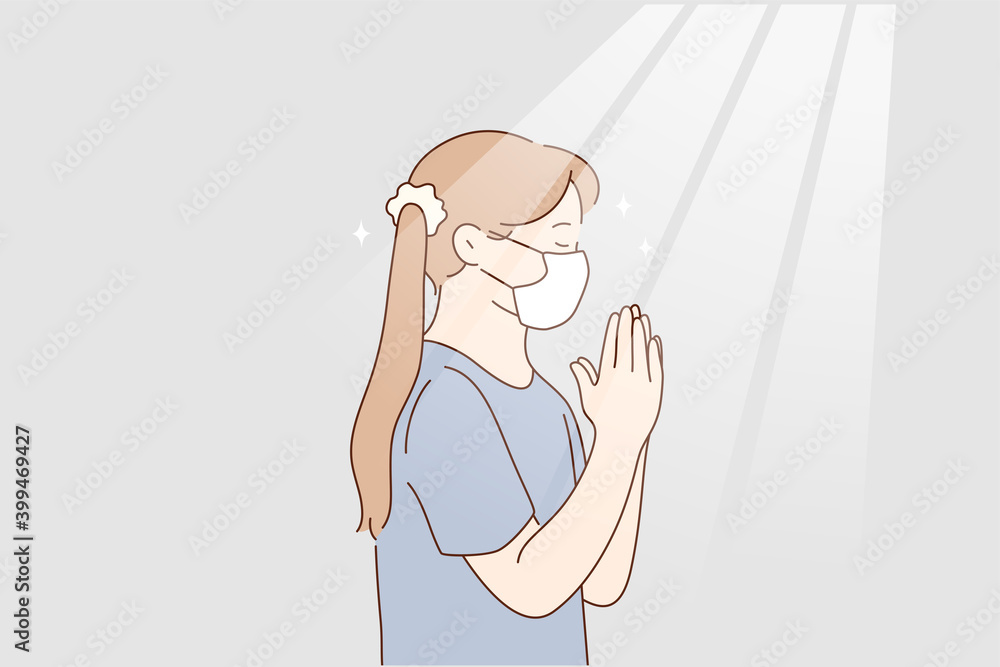 Little girl praying at home during pandemic concept. Little girl in protective medical mask from coronavirus infection staying and playing god with eyes closed hoping to stop infection worldwide Little girl praying at home during pandemic concept. Little girl in protective medical mask from coronavirus infection staying and playing god with eyes closed hoping to stop infection worldwide