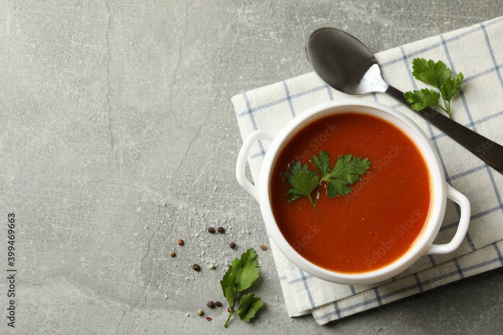 Bowl of tomato soup, spoon and towel on gray background Bowl of tomato soup, spoon and towel on gray background