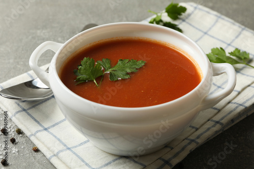 Bowl of tomato soup, spoon and towel on gray background