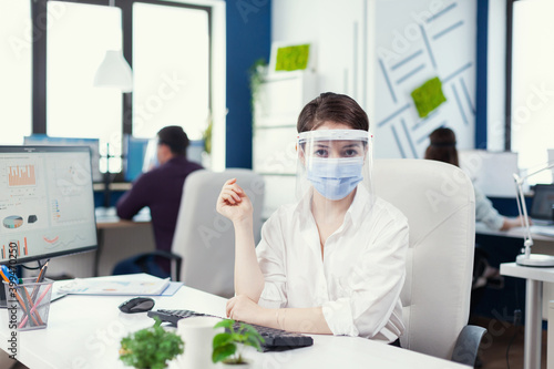Portrait of office worker wearing a face shield. Business team working in financial company respecting social distance during global pandemic.