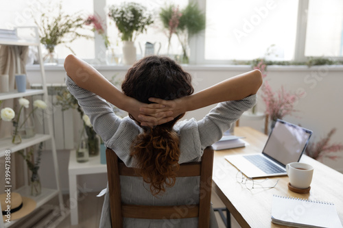 When all is done. Back rear view of happy young female florist sitting on chair in cozy studio pleased with work results. Creative interior designer stretching with hands behind head resting relaxing