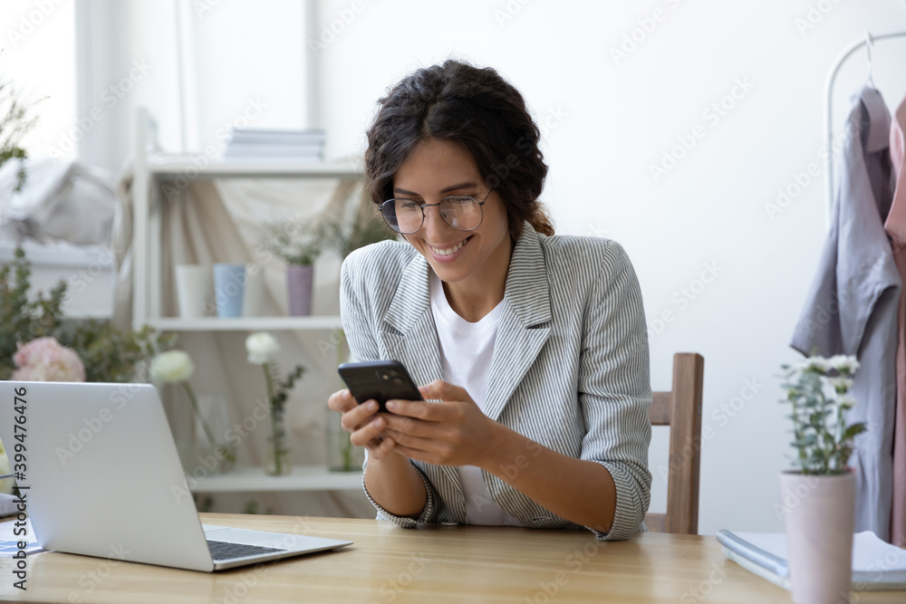 Good news. Excited young female self employed clothing designer sitting at work desk focused on mobile phone screen. Woman flower arranger reading email with profitable offer from potential customer Good news. Excited young female self employed clothing designer sitting at work desk focused on mobile phone screen. Woman flower arranger reading email with profitable offer from potential customer