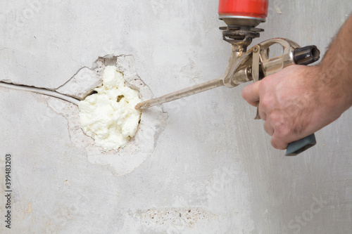 Canvas Print Young man hand using spray gun and filling hole with construction foam in concrete wall where was old outlet