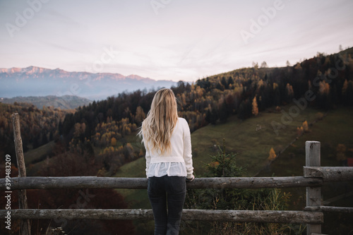 Traveler female standing near the fence and watching the sunset in the autumn mountains.