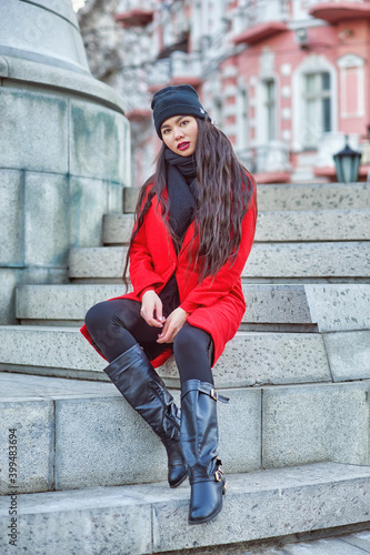 Obraz na płótnie Beautiful young woman of Asian appearance on a winter city street . A girl in a red coat and a knitted hat w salonie