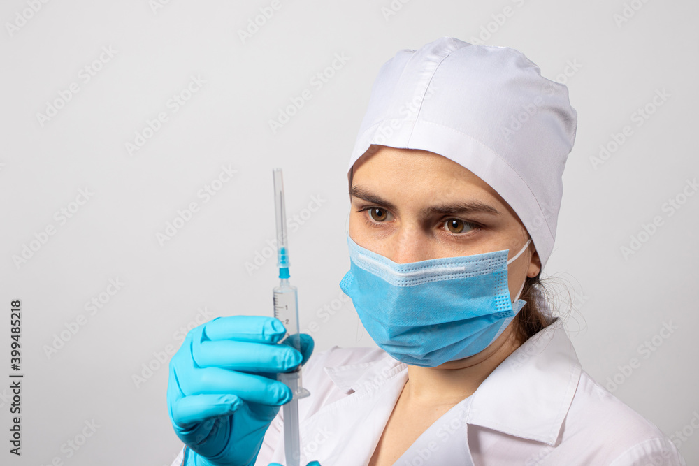 A nurse in a robe and a medical cap and gloves holds a syringe. Vaccination, Mantoux test and disease prevention, manipulation room in the clinic and hospital on a light background A nurse in a robe and a medical cap and gloves holds a syringe. Vaccination, Mantoux test and disease prevention, manipulation room in the clinic and hospital on a light background