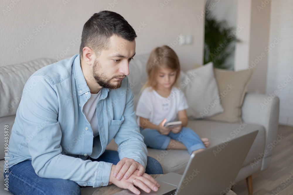 Father working from home with small child while in quarantine isolation during the Covid-19. Little girl looking on smartphone. 