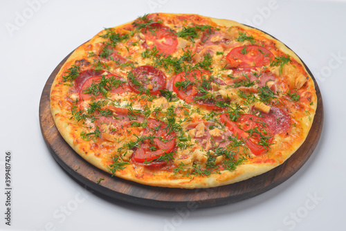 Pizza pollo with chicken meat, tomatoes and ham served on a round wooden board over white background.