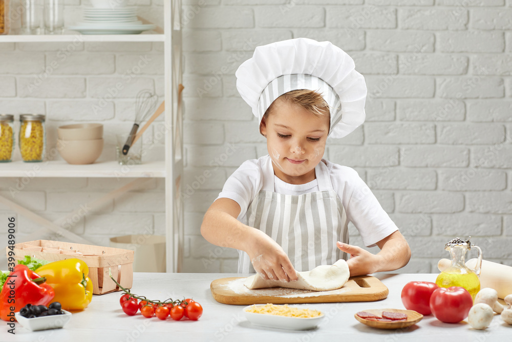 little child boy in cap and an apron knead the dough in the kitchen little child boy in cap and an apron knead the dough in the kitchen