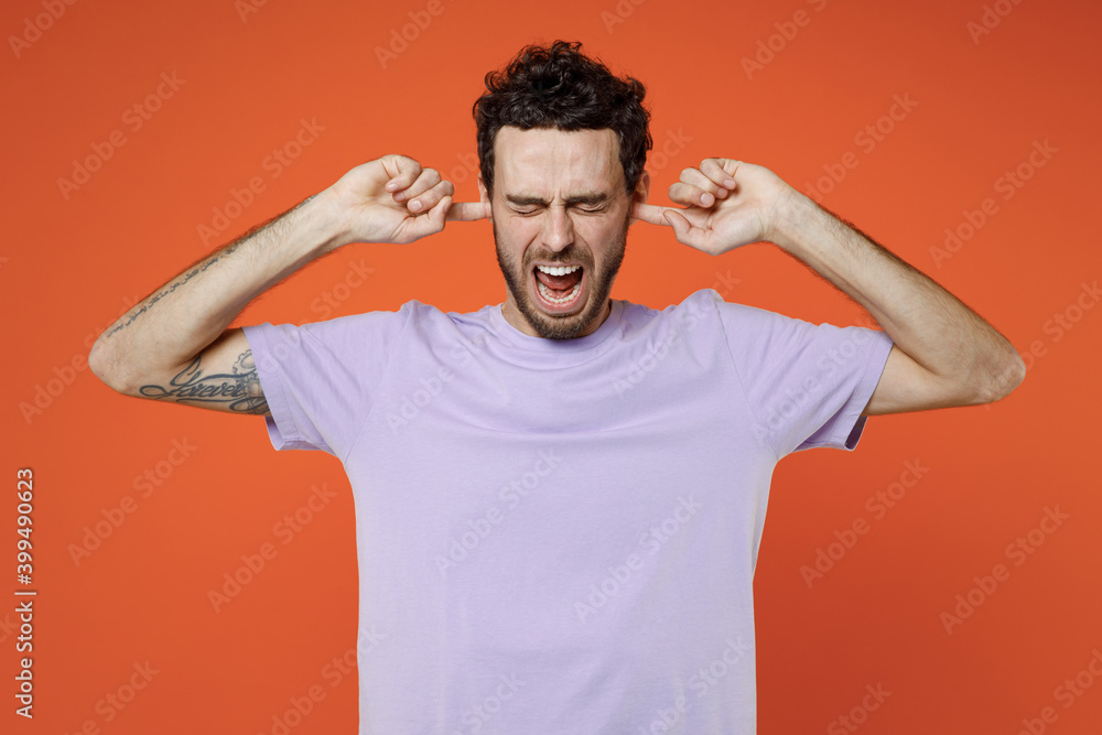 Frustrated crazy young bearded man 20s wearing basic casual violet t-shirt standing covering mouth with hands keeping eyes closed screaming isolated on bright orange color background studio portrait. Frustrated crazy young bearded man 20s wearing basic casual violet t-shirt standing covering mouth with hands keeping eyes closed screaming isolated on bright orange color background studio portrait.